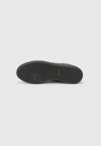 Black rubber shoe sole with a textured pattern. Features circular and hexagonal shapes for grip, with a slight curve at the heel.
