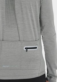 Grå cykeltrøje med tekstureret stof, lodret stribedesign og en lynlåslomme. Har logoet "PROTEST CYCLING" ved kanten.