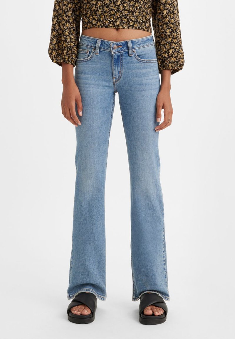 Light blue flared jeans made of denim, featuring a mid-rise waist and fading along the thighs. Paired with black sandals.
