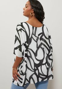 Top in stile kimono a motivi bianco e nero realizzato in tessuto trasparente, con una vestibilità comoda e maniche larghe, mostrato indossato di schiena.
