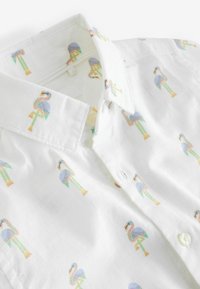 Weißes Kurzarmhemd mit Kragen, das ein Muster aus bunten Flamingos zeigt. Das Material wirkt leicht und leicht strukturiert.