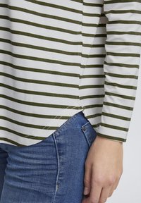 Langarmshirt mit weißen und olivgrünen Horizontalstreifen, mit abgerundetem Saum und seitlichen Schlitzen, kombiniert mit blauen Jeans.