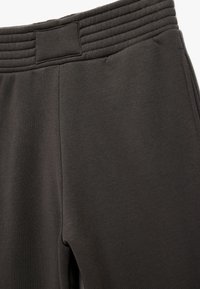 Mørkegrå sweatpants har et ribbet elastisk taljebånd og et glat, struktureret stof. Sømdetaljer løber langs siden af hver ben.
