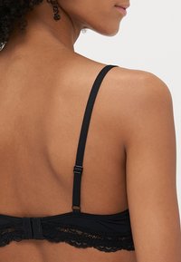 Reggiseno in pizzo nero con spalline regolabili, chiusura a gancio e occhiello, e orlo in pizzo a sardonicchio lungo la fascia. Tessuto morbido.