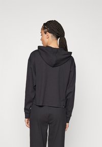 Felpa nera corta con un tessuto testurizzato a coste. Presenta un cappuccio con coulisse e maniche lunghe, abbinata a pantaloni coordinati.