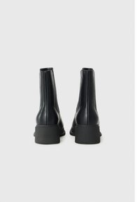 Botas de cuero negras hasta el tobillo con una textura suave, punta redonda y una suela gruesa de goma. Presentan un diseño sin costuras de altura media en el tobillo.