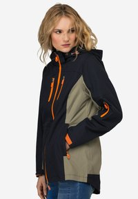 Giacca impermeabile con una combinazione di colori blu navy e khaki. Presenta zip arancioni, cappuccio regolabile e tasche con zip.