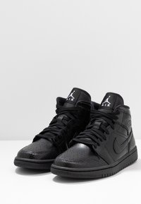 Mustat korkeat tennarit, joissa on teksturoitu nahkapinta, sileä varpaankotelo, silmiinpistävät nauhat ja logo kielekkeessä.