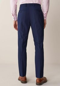 Pantalones navy de corte ajustado, con dos bolsillos traseros, pliegues sutiles y una textura suave. Unos zapatos marrones completan el look.