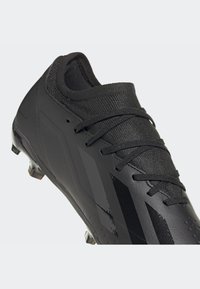 Scarpina da calcio nera con tomaia in sintetico liscio, dettagli texturizzati e colletto in maglia. Presenta lacci neri e una silhouette a profilo basso.