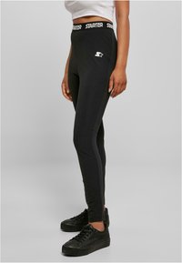 Fekete sport leggings fehér "Starter" logóval a derékrészen, testhezálló kialakítással és sima textúrával. Sötétebb árnyalatú kiegészítők.