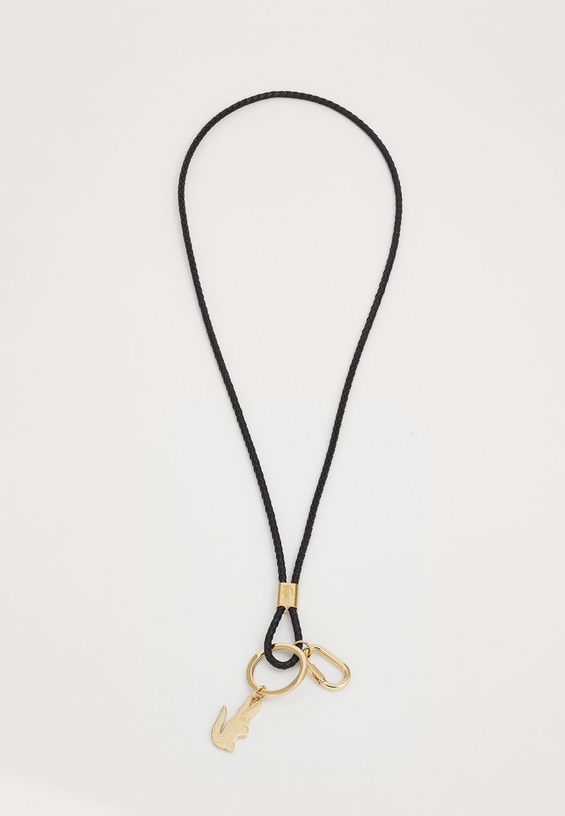 Černý pletený šňůrka s zlatým kováním, malým zlatým krokodýlem jako přívěskem a kovovou sponou pro uchycení.