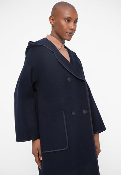 Palton din amestec de lână navy cu glugă, design cu două rânduri de nasturi, nasturi mari și buzunare frontale. Prezintă mâneci largi și detalii cu contrast.