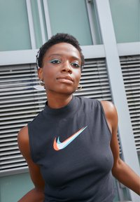 Čierny bezrukávový top Nike s vysokým golierom, so šikmým logom v oranžovej, modrej a bielej farbe. Hladký bavlnený materiál.
