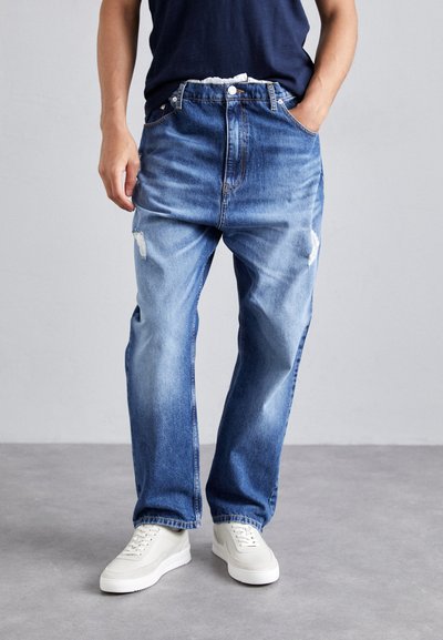 Light blue denim jeans with a loose fit, featuring two front pockets, a ripped detail on the left thigh, and a button fly.