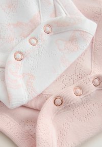 Primo piano di abbigliamento per neonati rosa e bianco con motivi lavorati a maglia e bottoni automatici color oro rosa lungo i bordi.
