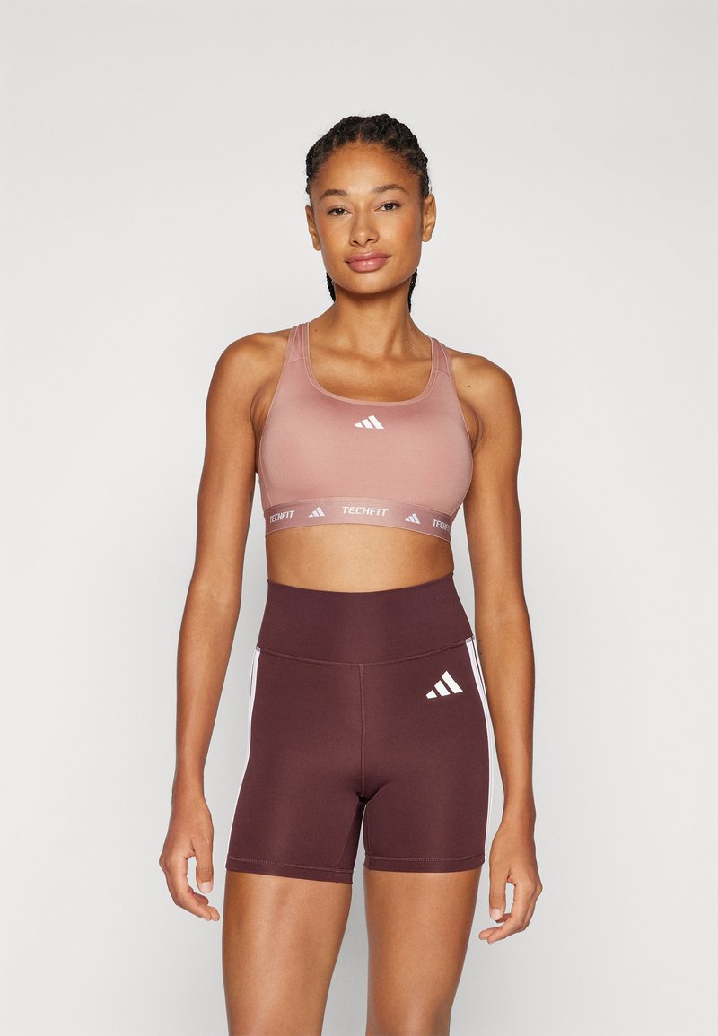 Sport-BH i gradient rosa med hvite striper, paret med høyt liv burgunder shorts med hvite detaljer og logo.