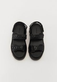 Black sandals with two adjustable Velcro straps, textured hexagonal pattern on straps, rounded toe, and rubber soles.