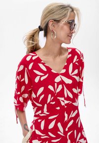 Rotes Kleid mit weißen Blättern, V-Ausschnitt, kurzen Ärmeln und Kordelzugdetails. Leichter Stoff mit lockerer Passform.