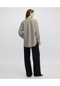 Camicia button-up a righe in beige e oliva con colletto e vestibilità ampia, abbinata a pantaloni larghi neri. Presenta maniche lunghe e polsini.