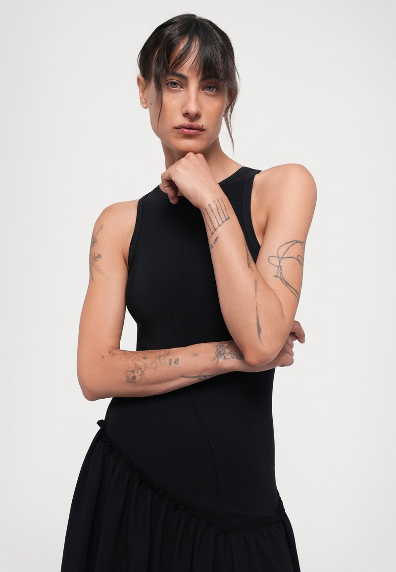 Black sleeveless dress with a fitted bodice and a gathered, flared lower section. Made of smooth fabric, featuring adjustable side details.