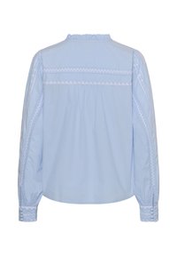 Blouse bleu clair à manches longues, avec des accents brodés blancs le long des épaules et des poignets, et un col froncé.
