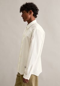 Biała koszula na guziki wykonana z bawełny, z klasycznym kołnierzem, długimi rękawami i prostym krojem. Subtelne logo na bocznym szwie.