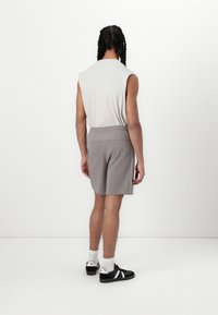 Shorts en sweat gris avec une taille élastique, vus de dos, accompagnés de chaussures noires et de chaussettes blanches. Tissu lisse et coupe décontractée.
