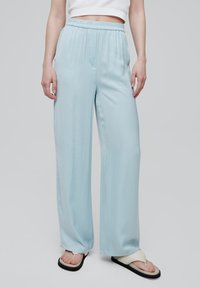 Lichtblauwe wijde broek met een elastische tailleband, een soepele textuur en zijzakken, gecombineerd met witte teenslippers met zwarte zolen.