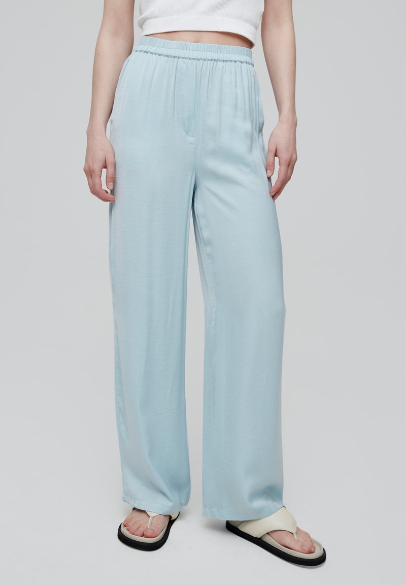 Lichtblauwe wijde broek met een elastische tailleband, een soepele textuur en zijzakken, gecombineerd met witte teenslippers met zwarte zolen.