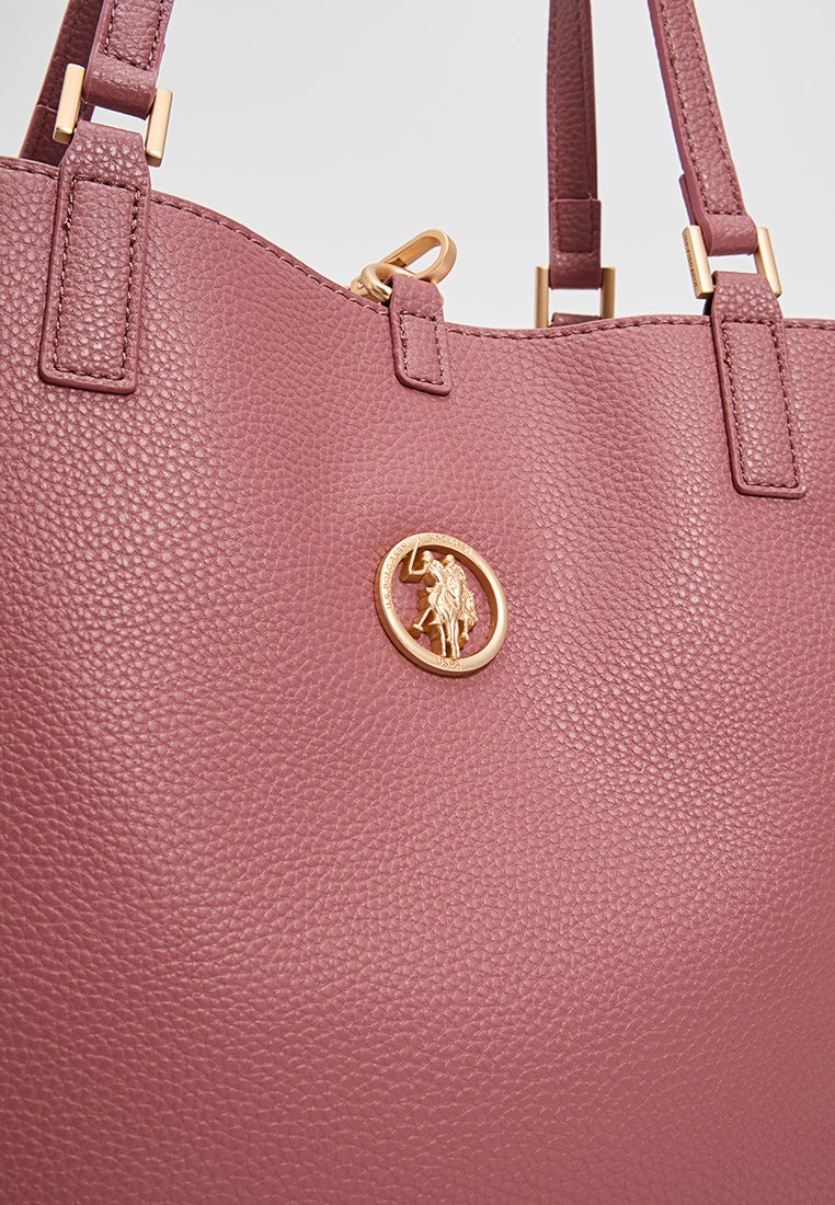 Tote bag en cuir rose texturé avec des détails en or et un emblème circulaire représentant un cheval et un cavalier. Deux poignées supérieures pour le transport.