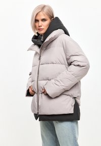 Vatteret jakke i lys grå med sort hætte, med lynlås foran, elastiske sider og to frontlommer. Glat tekstur og nutidigt design.