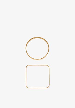 Zlaté kovové krúžky, jeden kruhový hore a jeden štvorcový s zaoblenými rohmi dole, na jednoduchom bielom pozadí.