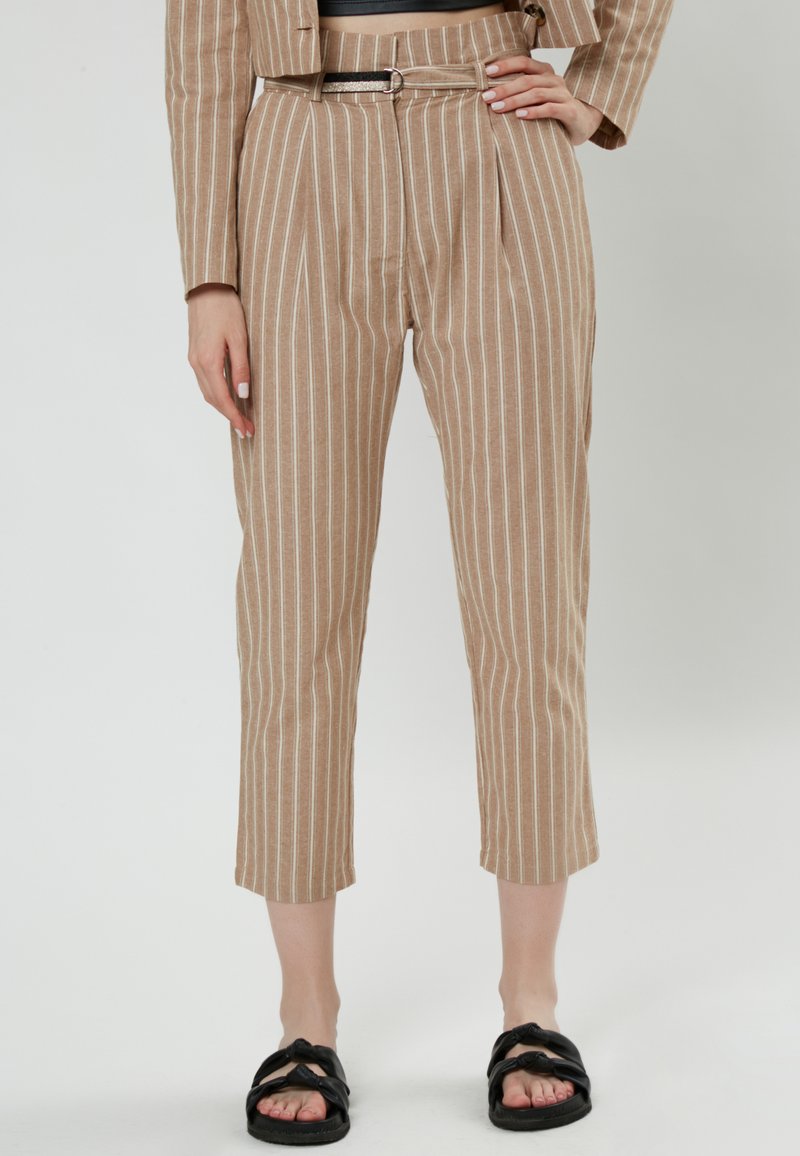 Pantalones a rayas en tono marrón, con pernera estrecha, pliegues en la parte delantera, cintura con cinturón y largo recortado, combinados con sandalias negras tipo slide.
