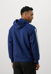 Felpa blu navy realizzata in materiale morbido, dotata di cappuccio, maniche lunghe e strisce laterali bianche. Dettaglio con polsini e orlo a costine.