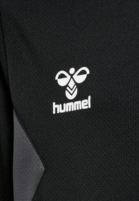 Maglietta sportiva nera con tessuto testurizzato, logo "hummel" bianco e un design stilizzato di un'ape al centro, con accenti grigi.