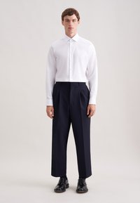 Witte lange mouwen overhemd met een klassieke kraag, gecombineerd met marineblauwe geplooide broek en zwarte veterschoenen. Minimalistisch ontwerp, gladde stof.