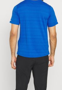 Modrá košile s krátkým rukávem, s horizontálními pruhy, kulatým výstřihem a černými kalhotami. Hladká textura a lehká tkanina.