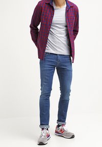 Röd och blå rutig flanellskjorta, grå t-shirt, blå jeans, grå och röda sneakers, stående pose, avslappnad passform.