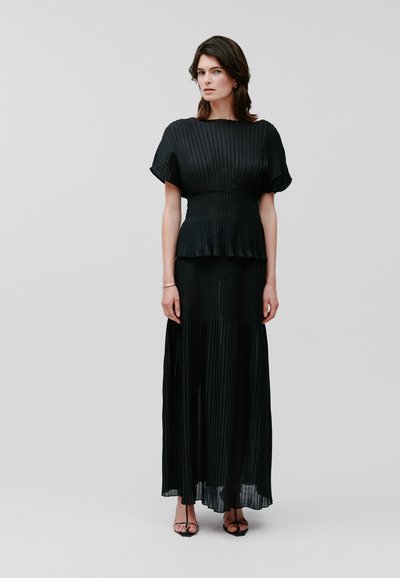 Rochie neagră plisată cu mâneci scurte, corset ajustat și fustă lungă. Fabricată dintr-un material ușor, având o textură fluidă și o siluetă elegantă.