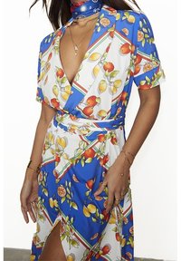 Robe fluide en tissu bleu vif avec un motif de fruits d'oranges et de citrons, décolleté en V profond, taille ceinturée et fente sur le côté.