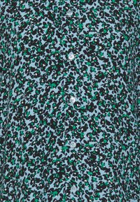 Multicolored blouse with a light blue background featuring a black and green leopard print pattern. Six white buttons down the front.