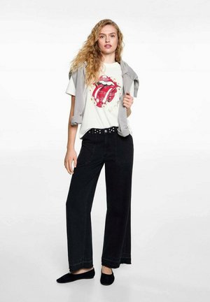 Grafische t-shirt met het rode logo van de Rolling Stones, gecombineerd met hoge taille zwarte wijde broek en een lichtgrijze trui die op de schouders is geknoopt.