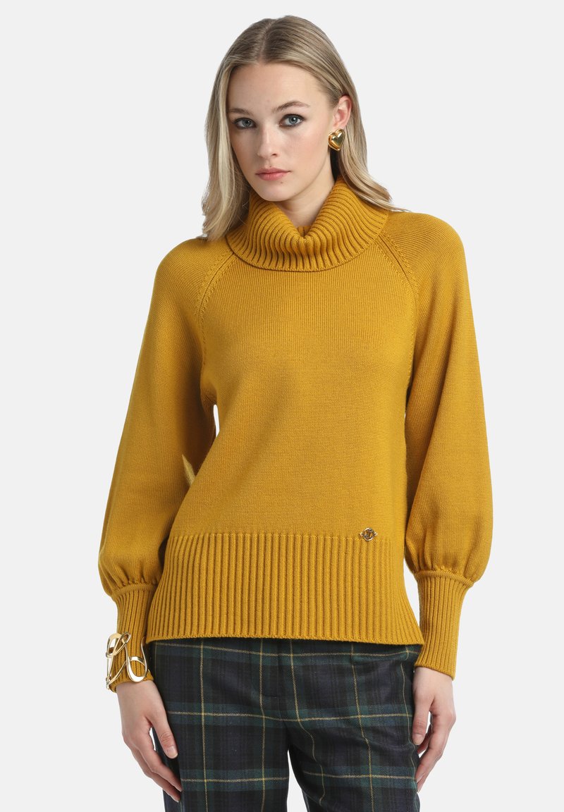Mustard yellow sweater with a high ribbed cowl neck, balloon sleeves, and ribbed hem, featuring a small branding detail near the bottom.