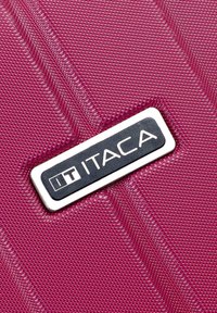 Material de equipaje texturizado en color púrpura con una placa del logo ITACA de color plateado brillante. Presenta un patrón diagonal de pequeños puntos en relieve.