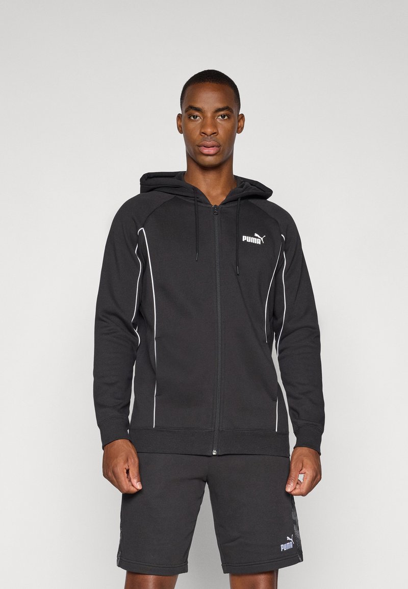 Svart zip-up hettegenser med hette, hvite aksentlinjer og en liten logo på brystet. Kombinert med matchende svarte shorts.