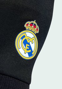 Crna tkanina s istaknutošću grba Real Madrida, koji se sastoji od plavog i žutog kružnog emblema s zlatnom krunom na vrhu.