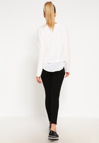 Bílý dlouhý rukáv top s texturovaným designem, vrstvený přes světle modrou košili. Spárováno s černými slim-fit kalhotami a černými botami.