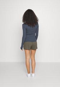 Long-sleeve navy ribbed top paired with olive green shorts, featuring a relaxed fit. White sneakers complete the outfit.