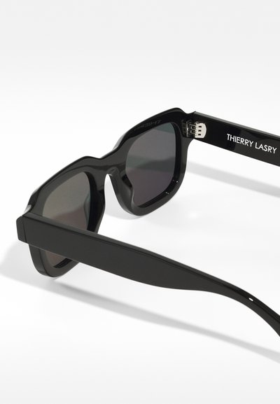 Ochelari de soare negri cu un cadru gros, având un finisaj mat și lentile de culoare gri. Numele brandului "THIERRY LASRY" este imprimerat pe braț.